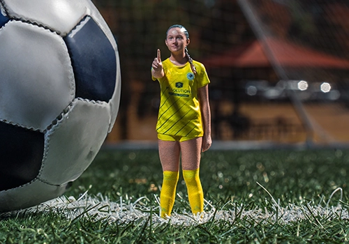 Miniature 3D-printed replica of a young soccer player standing next to a full-size soccer ball for scale